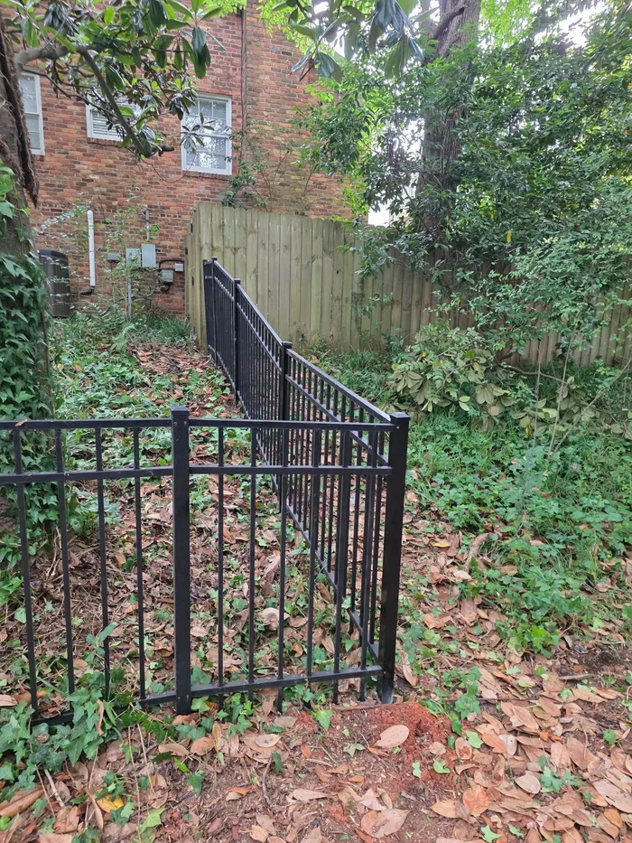 Aluminum fencing and gate stepping down a wooded slope beside a brick home